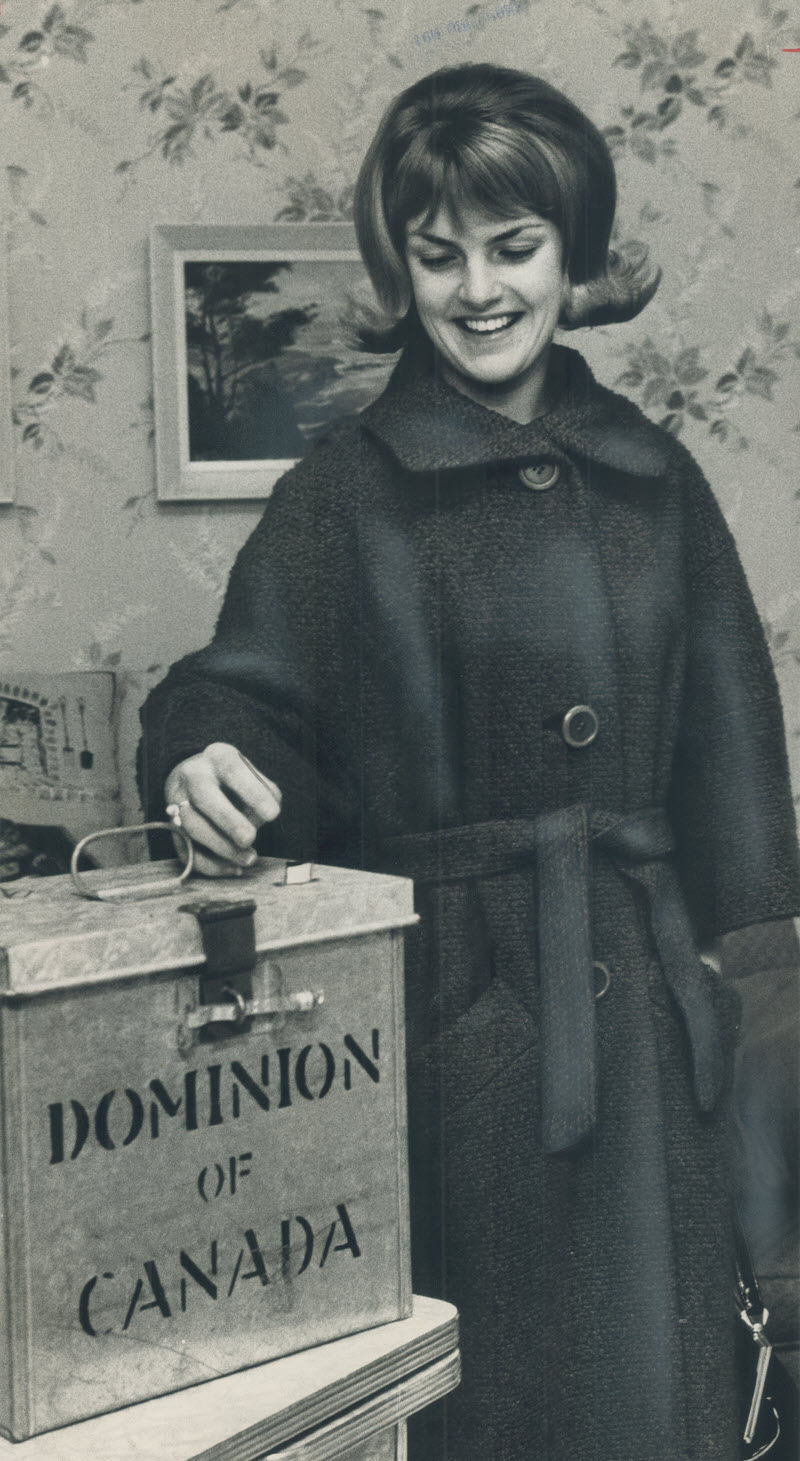 Black and white photo of a young smiling woman placing her ballot in a metal ballot box