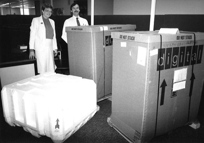 Black and white photo of a woman and a man standing behind two boxes that are nearly as tall as they are, with the word 'digital' written across the front