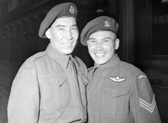 Black and white photo of two young First Nations men wearing military uniforms standing next to each other and smiling
