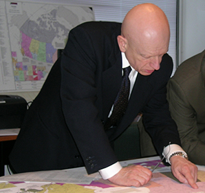 A bald middle-aged man peers down at a map of Canada set up on a table
