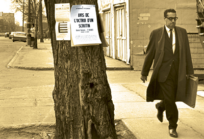Un homme portant un costume et un manteau long marche près d'un arbre sur lequel sont épinglés plusieurs documents, dont un « Avis de convocation »