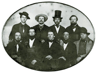Photo en noir et blanc de neuf hommes en costume répartis en deux rangées, face à la caméra. 