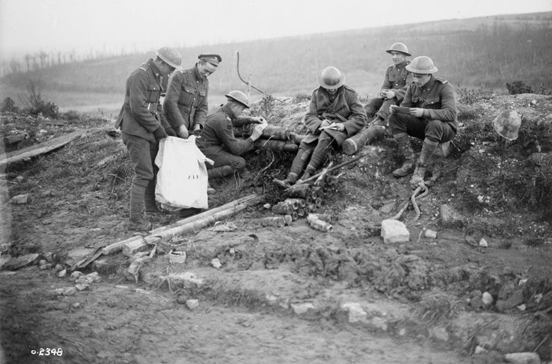 Photo en noir et blanc de six soldats dans leur uniforme de la Première Guerre mondiale, assis sur un monticule de terre, en train de remplir leur bulletin de vote.