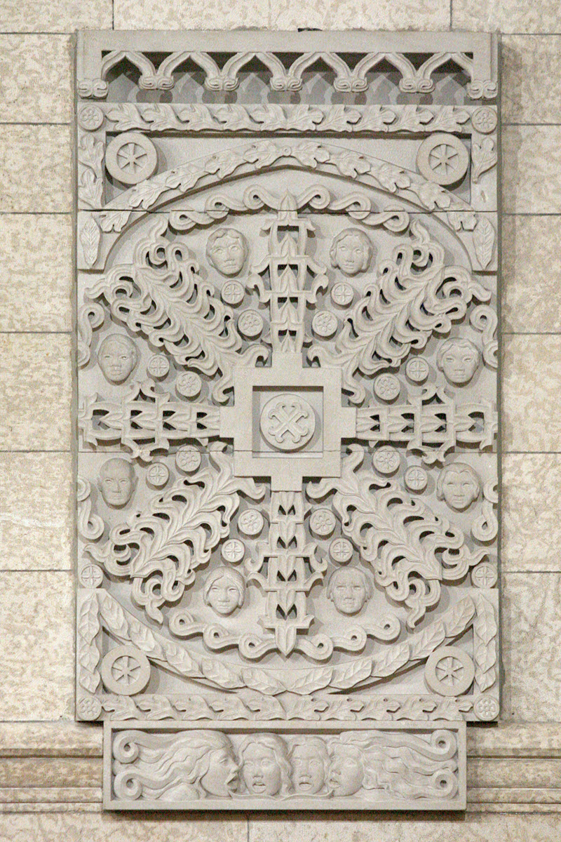 Panneau rectangulaire en pierre richement sculpté, avec un « X » au centre entouré de motifs décoratifs.
