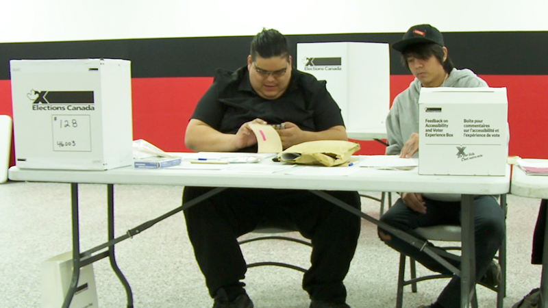 Photo de deux travailleurs électoraux assis à une table et remplissant des documents.